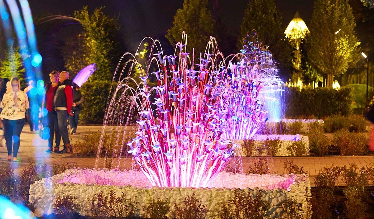 Public art with backlighting and decorative glass flower elements on a city alley at night