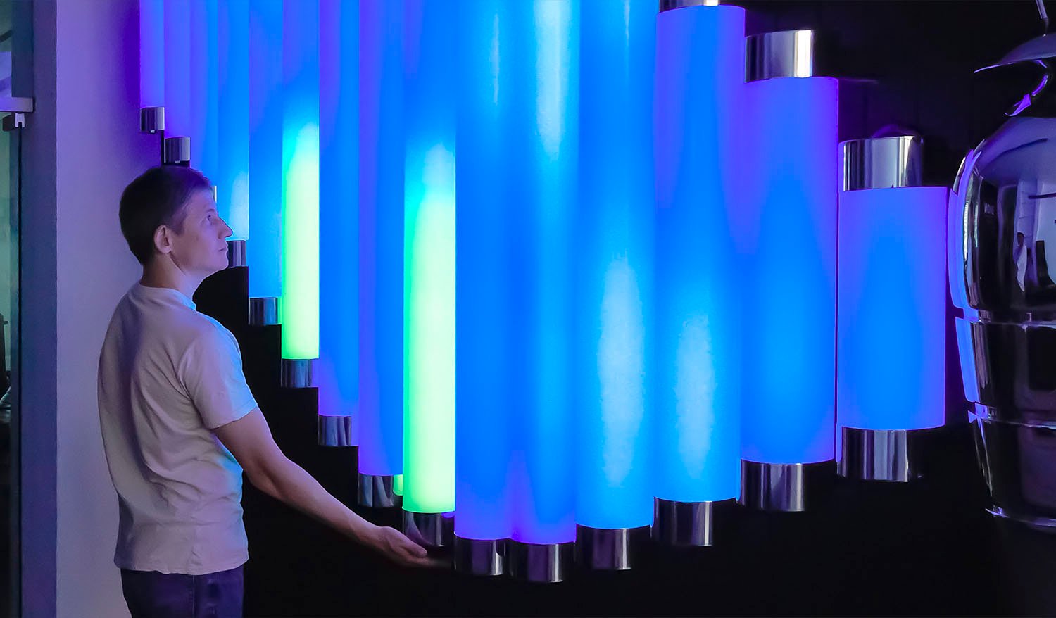 Visitor interacting with the Butterfly installation by touching glowing blue, turquoise, and green light tubes.